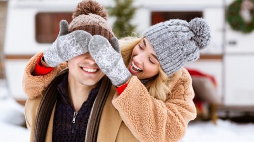 une femme avec un bonnet et des habits d'hiver obstruant la vision de son copain avec ses mains
