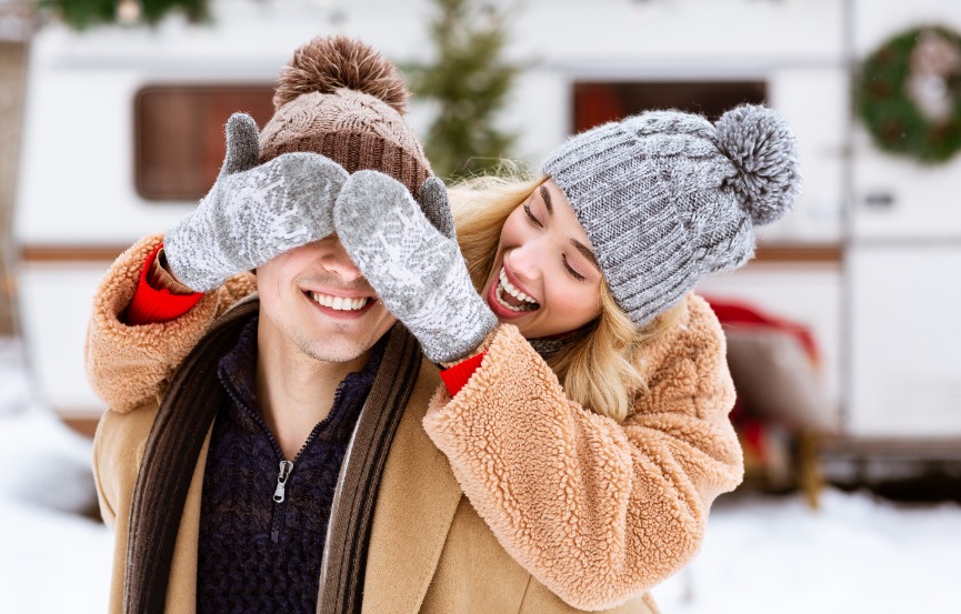 une femme avec un bonnet et des habits d'hiver obstruant la vision de son copain avec ses mains