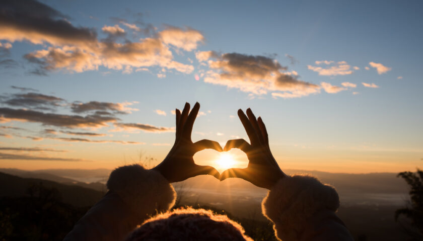 une personne formant un coeur avec ses mains pour montrer le soleil
