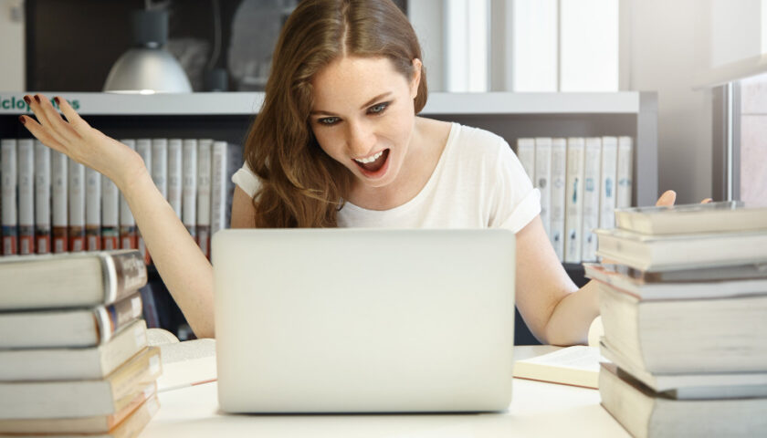 femme devant son ordinateur et des livres et qui ouvre la bouche