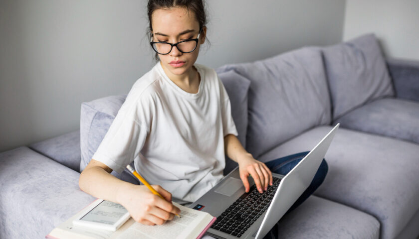 femme prenant des notes sur son canapé avec son ordinateur sur les genous